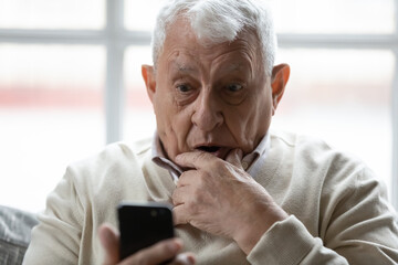 Surprised elderly 80s man using smartphone look at screen shocked by unexpected news or message,...