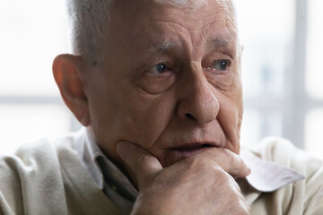 Close up of upset mature 80s man feel lonely look in distance mourning or yearning, sad pensive elderly 70s grandfather thinking pondering, distressed with solitude loneliness in retirement house