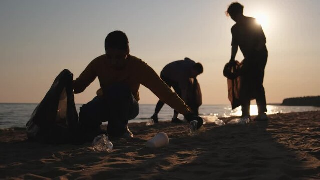 Earth day. Volunteers activists collects garbage cleaning of beach coastal zone. Woman and mans puts plastic trash in garbage bag on ocean shore. Environmental conservation coastal zone cleaning
