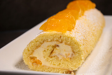 Delicious homemade mandarin cake roll with buttercream feeling, white plate and grey table background 