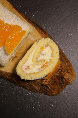 Delicious tangerine cake roll with vanilla buttercream filling on wooden plate, holiday winter dessert 