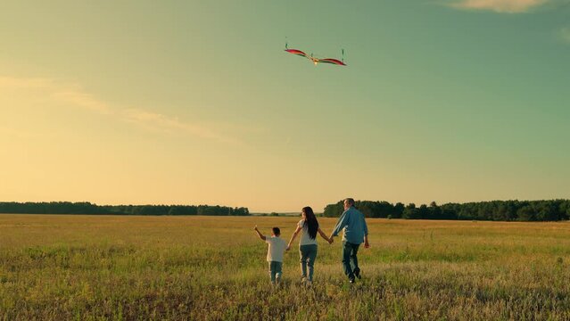 Young family is playing with kite in meadow. Happy family with baby in park playing with kite. Family walk on grass, child dreams of flying. Active people together travel to nature. Kid wants to fly
