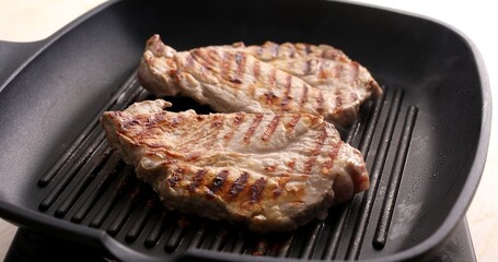 Pieces of raw meat on a grill pan. Frying steaks. Preparing food in the kitchen.