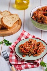 Eggplant caviar from baked eggplants, sweet peppers and tomatoes, seasoned with vegetable oil, on a green clay plate on a white wooden background. Eggplant recipes.