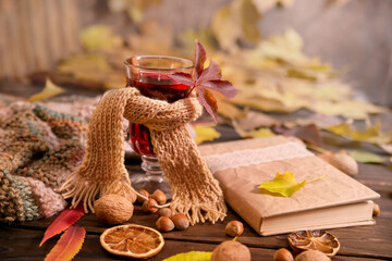 Autumn, autumn leaves, a glass of hot wine wrapped in a warm scarf on a wooden table background, a book, copy space. Seasonal drink, relaxing sunday and warmth and comfort concept. 