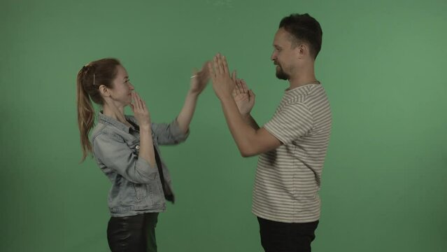 Young heterosexual couple playing clapping and having fun against green screen
