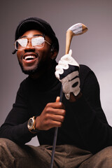 Portrait of smiling and elegant african american man in eyeglasses holding golf club isolated on grey - obrazy, fototapety, plakaty