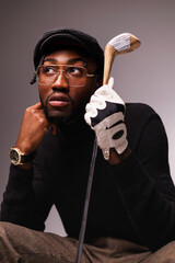 Portrait of elegant african american man in flat cap and glove holding golf club isolated on grey