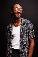 Portrait of stylish and smiling young african american man in eyeglasses, short-sleeves shirt and golden chain isolated on black