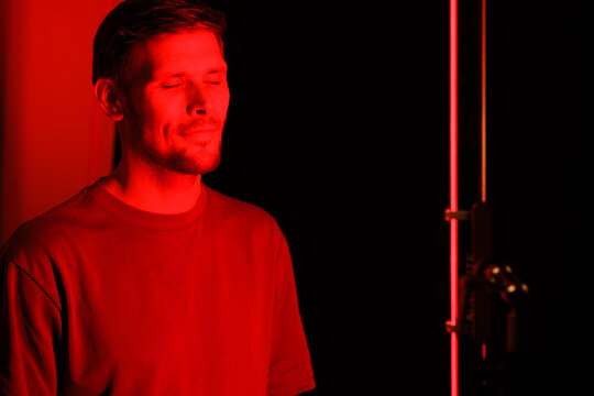 Embarking on red light therapy, the gentleman faces the camera in a portrait at a beauty salon, utilizing a red light device as a component of his anti-aging cosmetic treatment