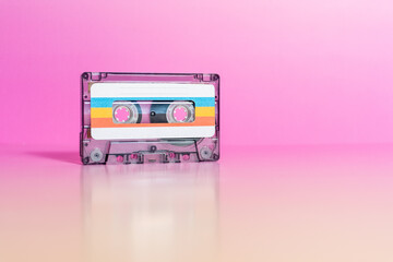 Transparent audio cassette with labels on fuchsia background.