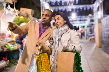 Happy married couple point finger at selected christmas tree decorations at street market