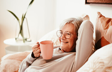 Portrait of happy relaxed handsome senior woman in bed holding a coffee cup, retirement lifestyle