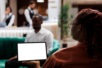 Woman tourist holding tablet in lobby at hotel reception, sitting in lounge area with device and white screen template. Person using blank display with isolated chroma key, front desk.