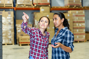 Two latina women workers of warehouse discussion working process pointing to something