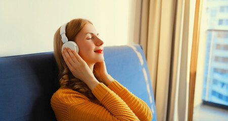 Happy relaxed young woman listening to music with wireless headphones with closed eyes lies on the...
