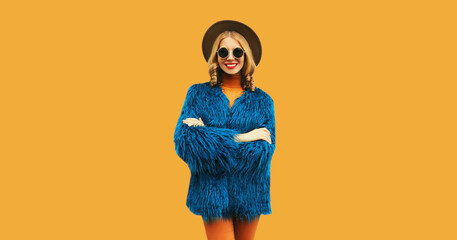 Stylish luxury happy young woman, female model posing wearing blue faux fur, round hat on yellow...