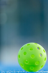 A pickleball ball in a blue court, defocused background