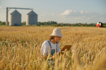 Naklejka na ściany i meble Smiling woman agronomist with tablet in a wheat field checks the harvest. High quality photo