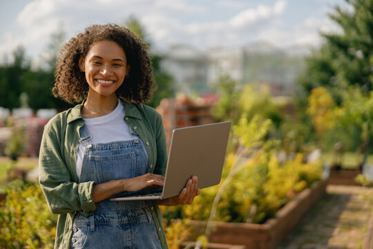 Woman gardener working on laptop while sitting on background of shop plants center