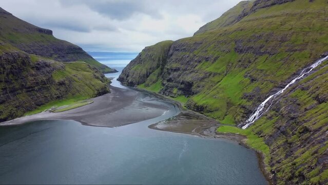 4k aerial drone footage of stunning Saksun fjord on Faroe Islands. Waterfall falling down from green hills into fjord. Saksun, Faroe Islands, Denmark, Europe