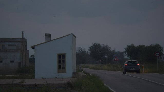 A car with headlights on drives down a suburban road past empty houses in the evening
