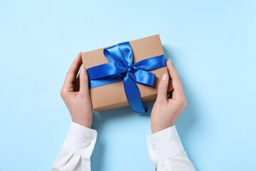 Woman holding gift box on light blue background, top view