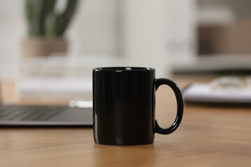 Black ceramic mug on wooden table at workplace - obrazy, fototapety, plakaty
