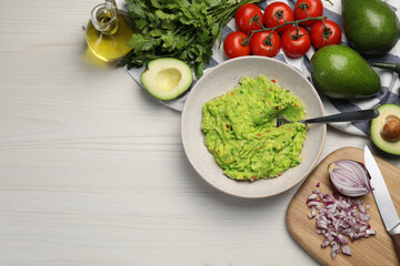 Delicious guacamole in bowl and ingredients on white wooden table, flat lay. Space for text