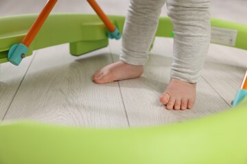 Cute little boy making first steps with baby walker on wooden floor, closeup