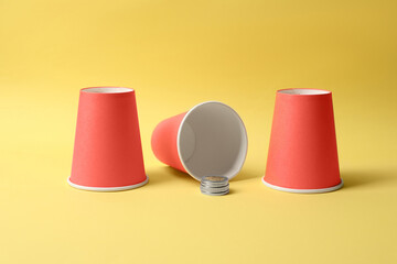 Three red cups and coins on yellow background. Thimblerig game