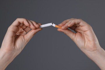 Stop smoking concept. Woman breaking cigarette on gray background, closeup