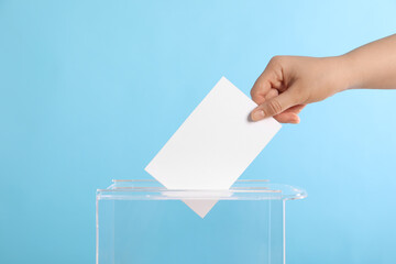 Woman putting her vote into ballot box on light blue background, closeup