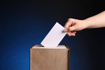Woman putting her vote into ballot box on dark blue background, closeup