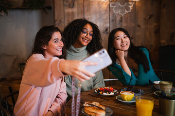 A group of smiling young women taking a selfie photo with a smart phone. They are having a brunch.