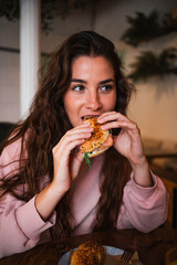 Beautiful young woman eating a bagel sandwich in a modern coffee shop.