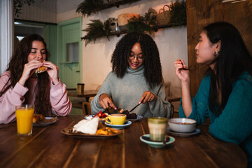 Three young women having fun during a brunch in a coffee shop. They are speaking to each other.