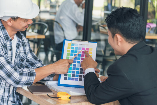 Asian interior designer team partner engineer brainstorming choosing color swatch. Engineer man Contractor brainstorming teams partner meeting together in office desk. Paint palette architecture plan