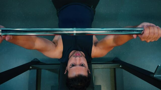 Top view of Asian man strong sweaty muscular athlete fit active man doing hardcore bench press with heavy barbell weights in the gym. Active male bodybuilder workout and crossfit training