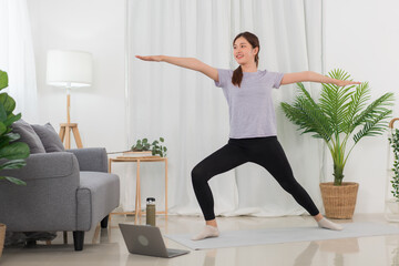 Yoga exercise concept, Young Asian woman watching yoga tutorial online to doing warrior pose on mat