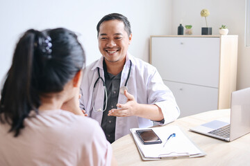 Friendly Asian male doctor during medical consultation with female patient at hospital 