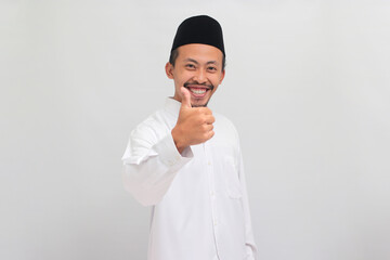 Confident young Indonesian man, wearing a songkok, peci, or kopiah, showing a thumbs-up gesture,...