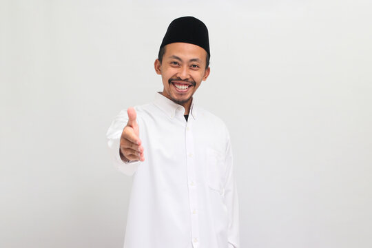 Confident young Indonesian man, wearing a songkok, peci, or kopiah, is ready to shake hands, isolated on a white background