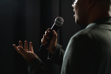 Confident successful speaker man talking on stage with spotlight strike through the darkness at corporate business event. Public speaker giving talk at conference hall. Stand up comedian.