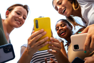 Low angle view of happy multiracial group of young women friends looking at mobile phone.