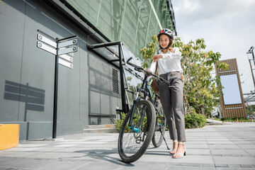 Asian young businesswoman standing with bicycle checking time on city street in morning before go to work at office, portrait smiling woman check watch, Commute to work, lifestyle biker