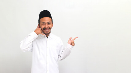 Excited young Indonesian man wearing a songkok or peci or kopiah, makes a call me gesture while...