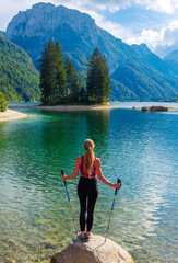 Hiker young female standing on rock enjoying beautiful lake and alps mountain- Italy, Lago del Predil- travel, sport,tourism in Europe