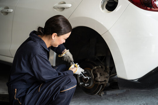 Hardworking female mechanic changing car wheel in auto repair workshop. Automotive service worker changing leaking rubber tire in concept of professional car care and maintenance. Oxus