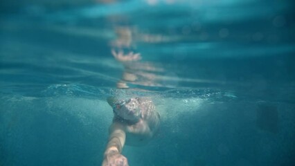 Underwater view of professional swimmer training in swimming pool, 4k 120 fps super slow motion raw video. Triathlete swim in black wetsuit 